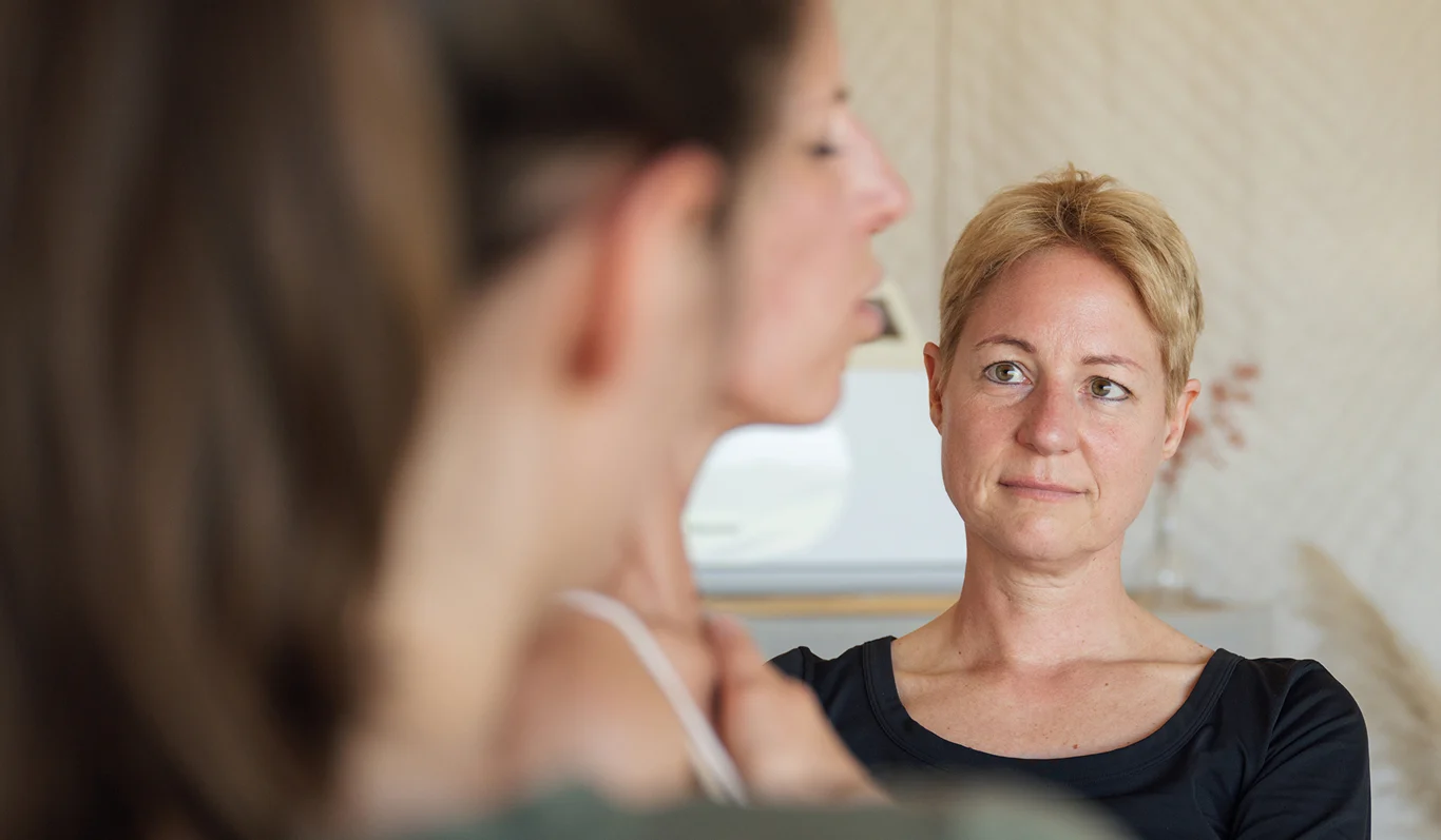 Zwei Frauen im Gespräch, eine hört aufmerksam zu, während die andere spricht, in einem modernen Raum.